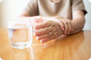 Elderly woman steadying her left hand with her right hand so she can pick up a glass of water.